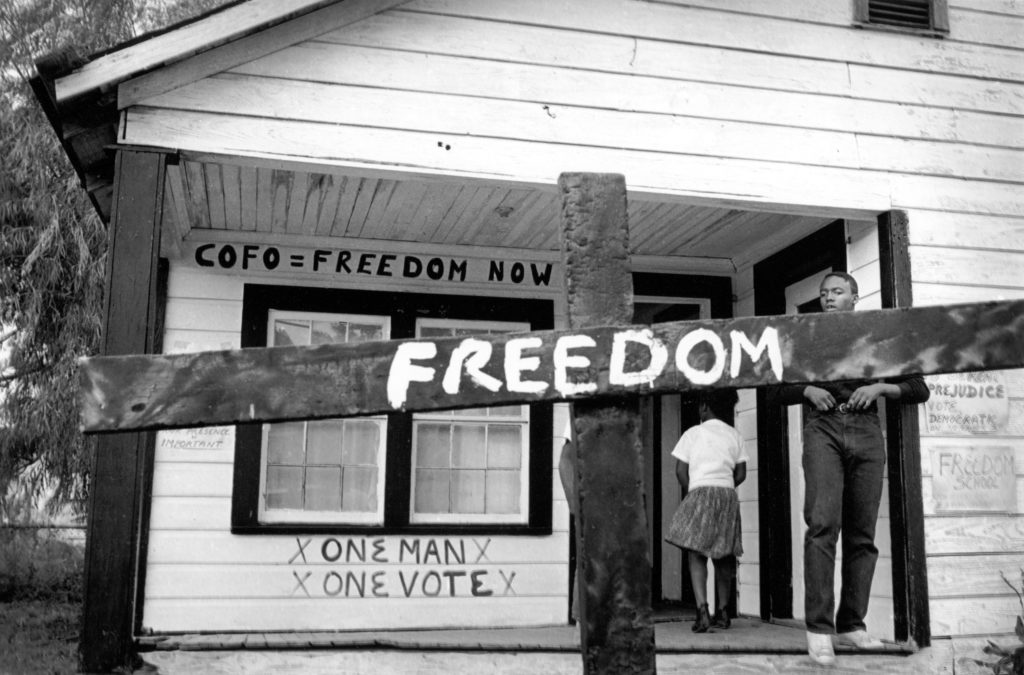 After the Ku Klux Klan burned this cross in front of a Mississippi Delta Freedom House, a civil rights worker transformed it with a painted message. Tamio Wakayama Indianola, Mississippi, 1964